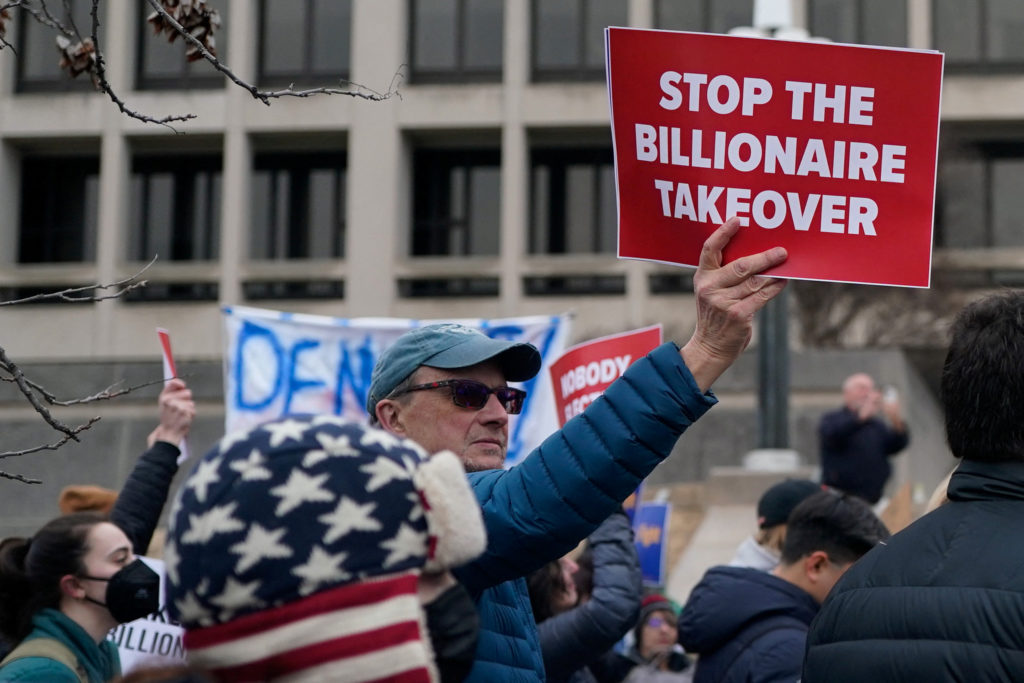 Man holds up a sign at a protest of DOGE firings of government workers.